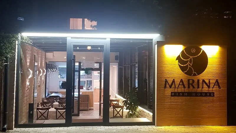 Marina Fish House at night: glass front, warm light and the round fish sign